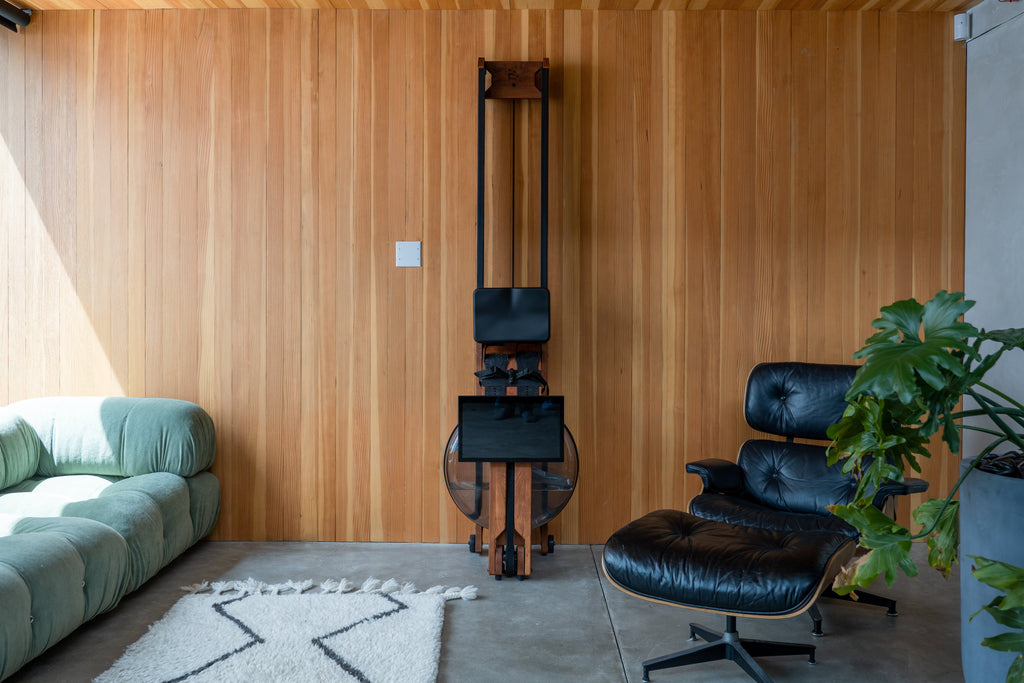 Ergatta WaterRower in upright position in a living room stored by a green couch and plant